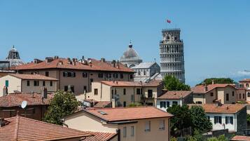 Blick auf eine historische Stadt mit traditioneller Architektur und dem schiefen Turm von Pisa im Hintergrund.