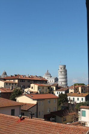 A view of a town with traditional buildings and a prominent tower with a leaning spire. - Attico sulla Torre (Pisa)