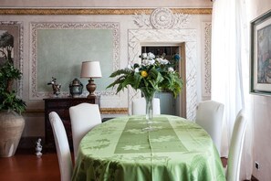 A dining room with a green tablecloth, white chairs, a vase of flowers, and a lamp on a side table. - Attico sulla Torre (Pisa)
