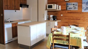 Une cuisine compacte dotée de meubles en bois, d’un four à micro-ondes, d’une machine à café et d’un coin repas avec une table dressée pour quatre personnes.
