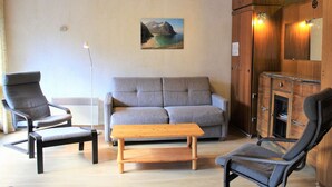 Un salon comprenant un canapé, deux fauteuils, une table basse en bois et un tableau accroché au mur.