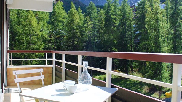 Un balcon avec une table et des chaises, donnant sur une forêt et des montagnes.