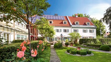 Un edificio de estilo europeo tradicional con tejado de tejas rojas, paneles solares y un jardín bien cuidado con rosales y setos.