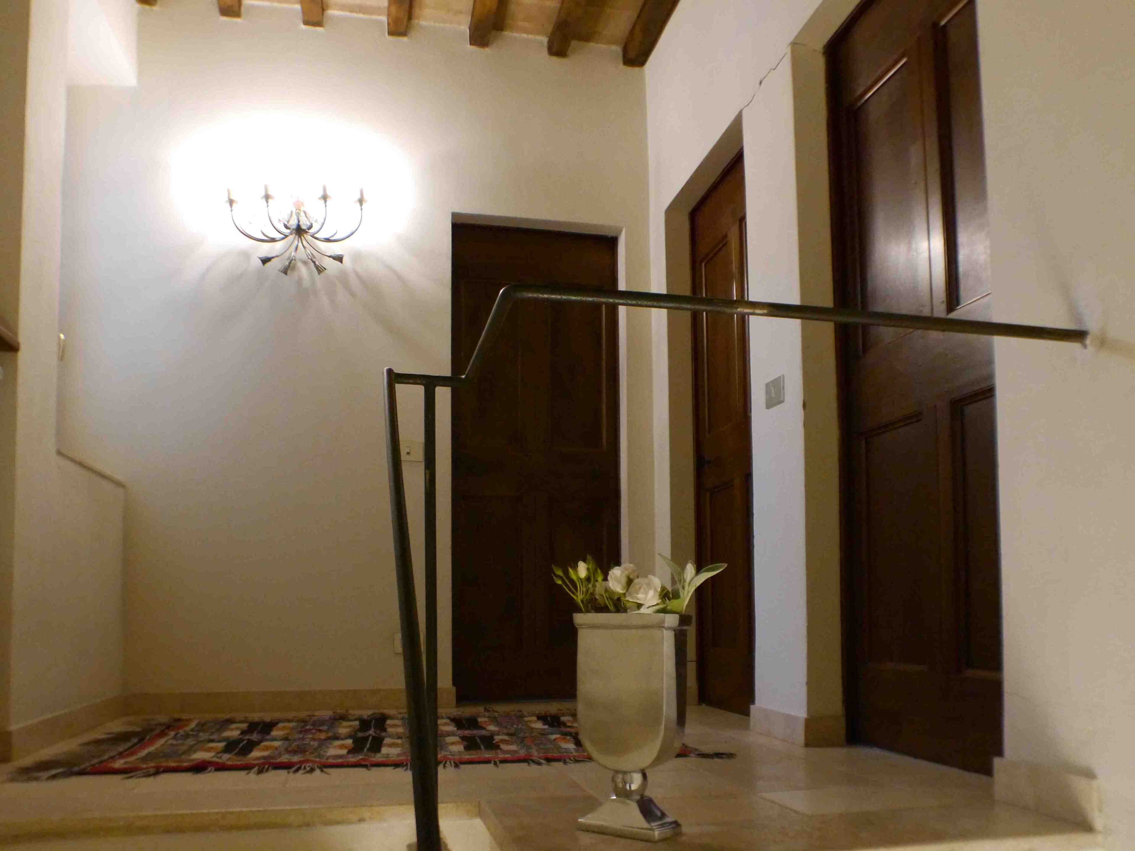 Un passadís amb una làmpada penjant, un vas amb flors i portes de fusta.