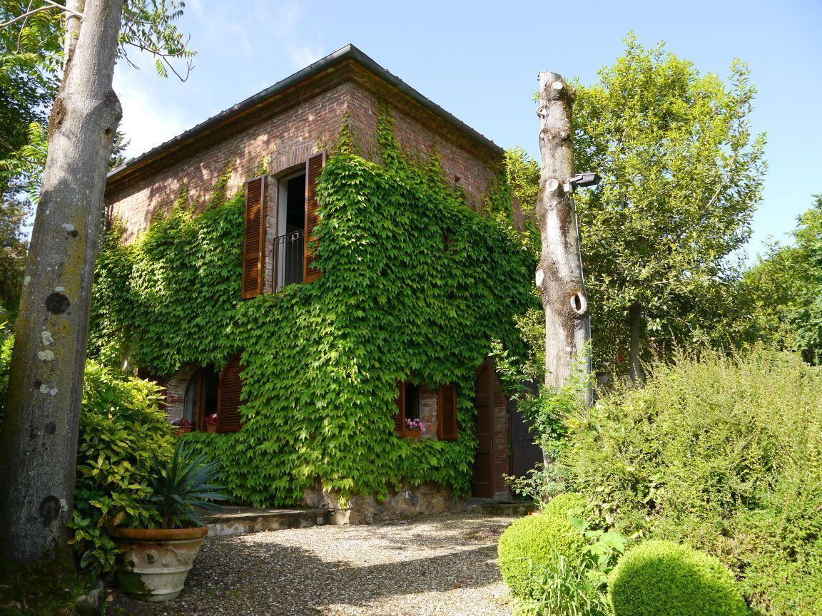 Un bâtiment rustique aux murs couverts de lierre, avec une allée gravillonnée et un jardin bien entretenu.