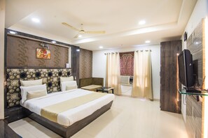 A modern hotel room with a large bed, a ceiling fan, a flat-screen TV, and a bathroom with a shower curtain. - Hotel Morya Regency (Bhopal)