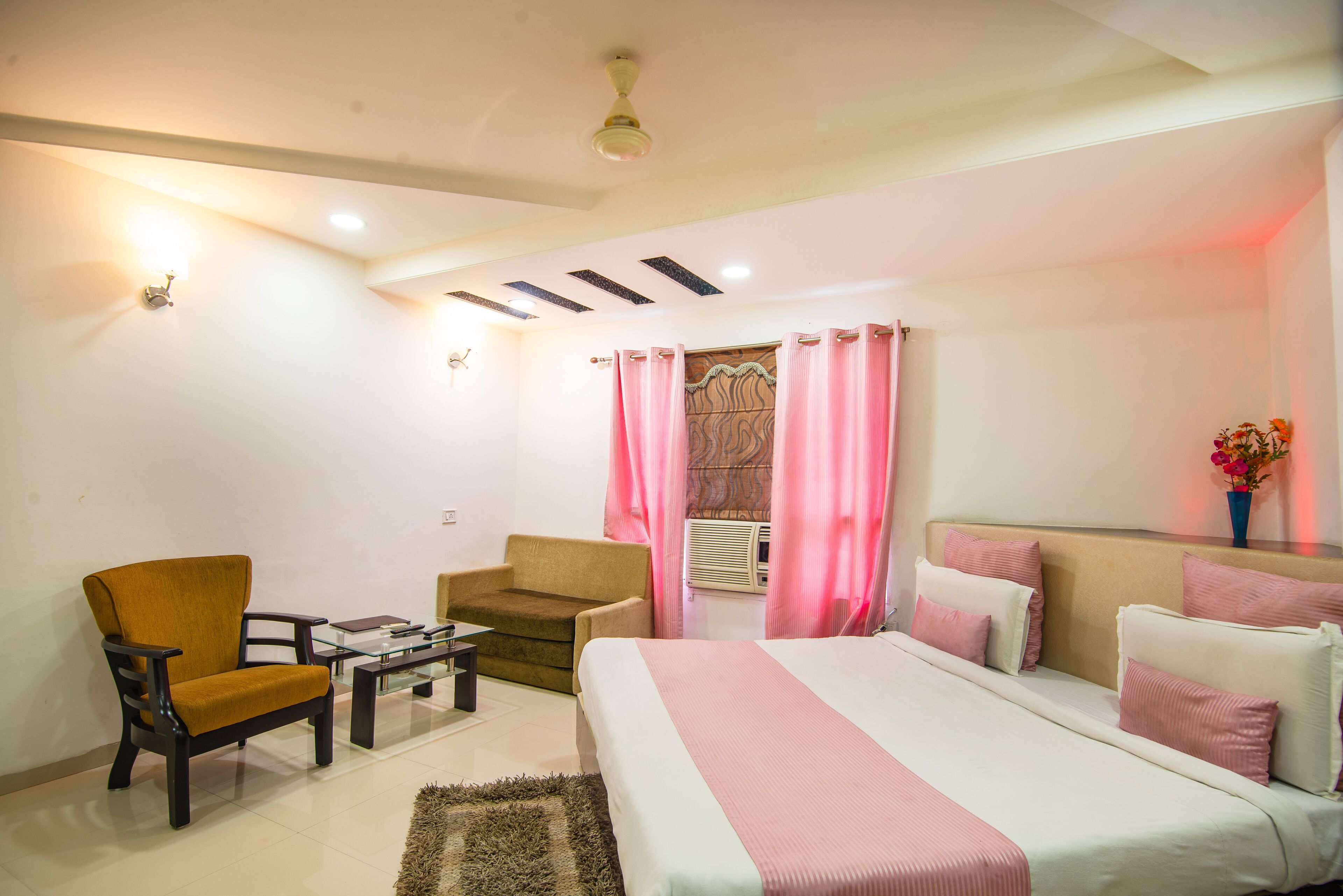 A modern hotel room with a bed, sofa, armchair, and a small table.