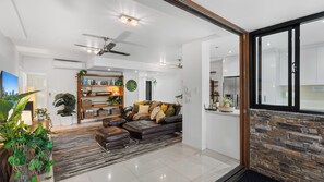 A modern living room with a leather sofa, a bookshelf, and a large window. - Luxury Pool Side Apartment in Beachfront Resort (Cairns North)