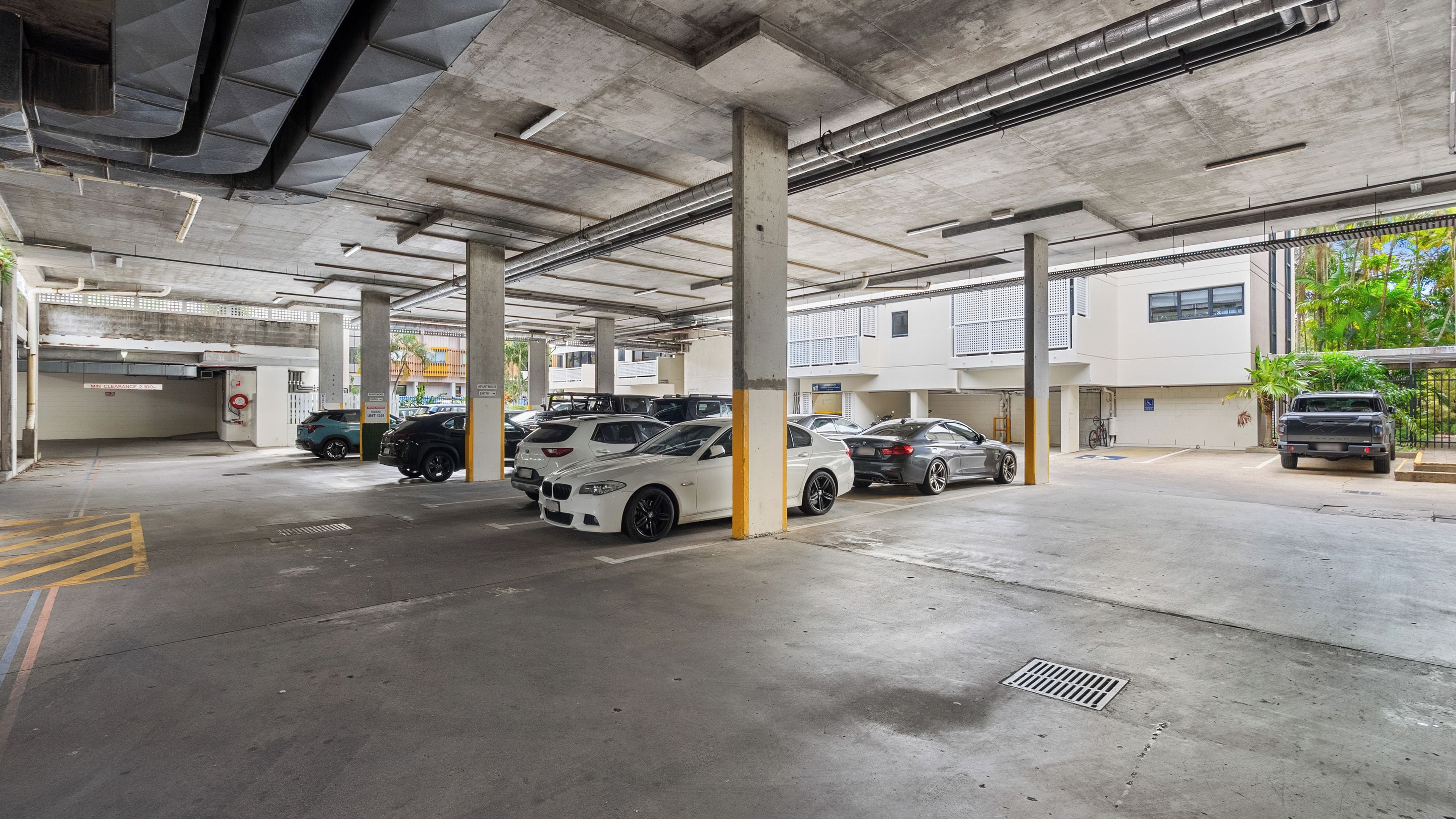 Un parking à plusieurs niveaux, avec des piliers en béton, plusieurs voitures garées et un immeuble doté de fenêtres et d’un balcon.