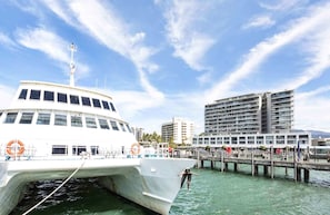 A white boat docked at a pier with a cityscape in the background. - Luxury Pool Side Apartment in Beachfront Resort (Cairns North)
