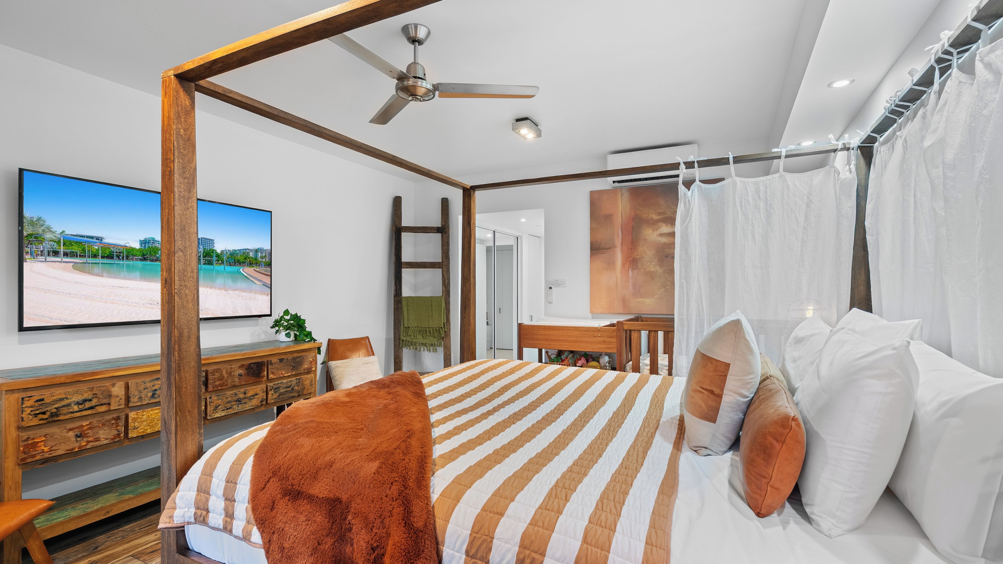 A bedroom with a bed, a ceiling fan, a desk, and a view of a beach.