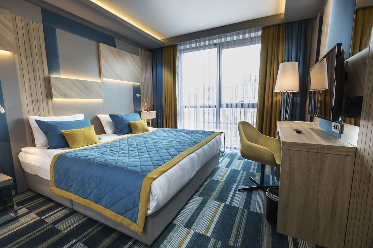 A modern hotel room with a large bed, a desk, and a TV.