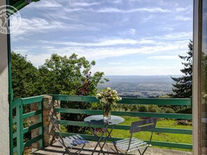 A balcony with a table and chairs, a vase with flowers, and a view of the countryside.