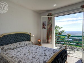 A bedroom with a bed, a nightstand, a window with a view, and a balcony with a table and chairs.