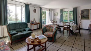 Ett rymligt vardagsrum med en grön soffa, en blommönstrad fåtölj och en matplats med ett bord dukat för fyra personer.