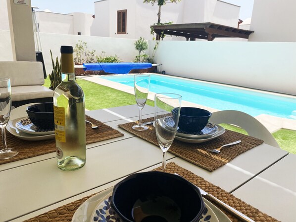 Ein Esstisch draußen mit Flasche, Gläsern und Schüsseln, mit Blick auf einen Swimmingpool.
