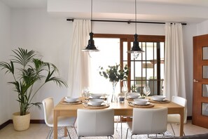 A dining area with a wooden table, white chairs, and hanging pendant lights.