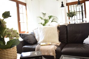 A living room with a brown leather sofa, a white throw blanket, a woven plant pot, and a small table with a book.