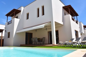 A modern two-story building with a pool, outdoor seating, and a covered patio area.