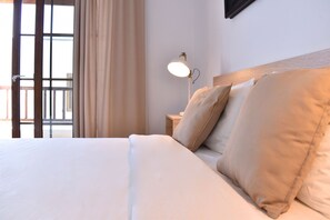 A bed with white bedding, a nightstand with a lamp, and a view through a window with curtains.