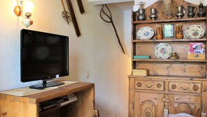 Une pièce comprenant un bureau en bois, une télévision, une chaise et une étagère ornée d’assiettes décoratives et d’un animal en peluche.