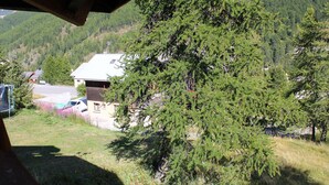 Un chalet de montagne avec un toit en pente, entouré d’une forêt dense et offrant une vue dégagée sur la vallée en contrebas.