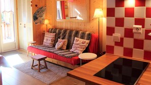 Une pièce chaleureuse avec un canapé, une petite table, un banc et un coin cuisine doté d’un crédence à carreaux.