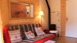 Une pièce chaleureuse avec un mur en bois, un canapé rouge orné de coussins à motifs, un petit tabouret en bois, une table blanche et une lampe.