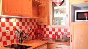 Une cuisine avec des meubles en bois, un crédence à carreaux rouges et blancs, un four à micro-ondes, une machine à café et une fenêtre donnant sur un paysage verdoyant.