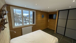Una camera da letto con una grande finestra, pareti in legno, un letto, un termosifone e una televisione.