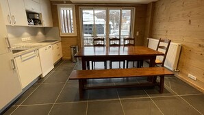 Una cucina moderna con zona pranzo, caratterizzata da un tavolo di legno grande, elettrodomestici integrati e vista attraverso le porte in vetro.