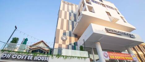 A modern building with a checkered facade, a visible coffee shop named "DII COFFEE HOUSE" at the ground level, and a sign for "ANGELIC ROYAL" on the upper floor.