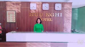 Un comptoir d’accueil d’hôtel avec un mur recouvert de panneaux en bois, trois horloges et un panneau indiquant les différents types de chambres et leurs prix.