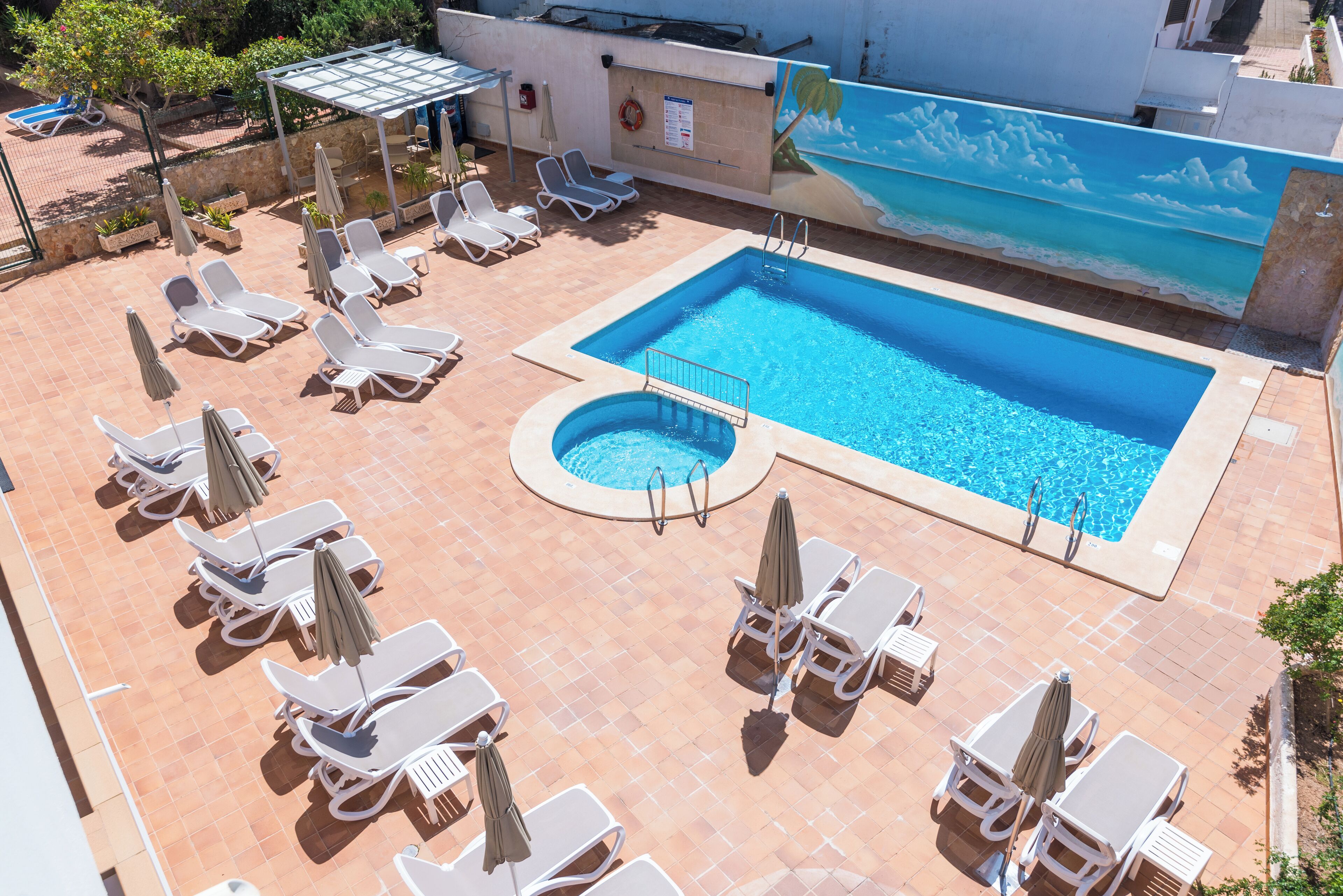 A rooftop pool area with multiple sun loungers and umbrellas, a small circular pool, and a mural of a beach scene.