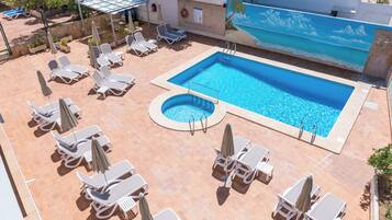 A rooftop pool area with multiple sun loungers and umbrellas, a small circular pool, and a mural of a beach scene.