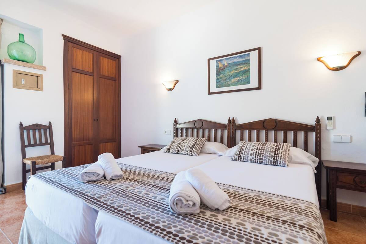 A hotel room with a large bed, two bedside tables, a wooden wardrobe, a chair, and a painting on the wall.
