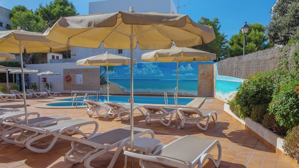 A poolside area with sun loungers and umbrellas, a lifebuoy, and a mural of a beach scene. - Hotel Ses Puntetes (Santanyi)