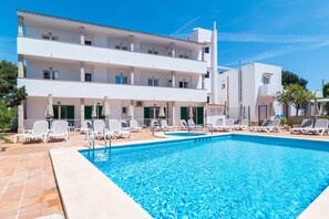 A swimming pool with white lounge chairs and umbrellas, a multi-story building with balconies, and a clear blue sky. - Hotel Ses Puntetes (Santanyi)