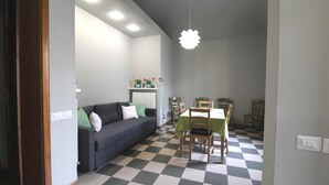 Una habitación con piso a cuadros, un sofá, una mesa de comedor con sillas y una lámpara colgante.