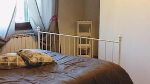 Un dormitorio con cama, una mesita de noche, una ventana con cortinas y un radiador.