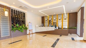 A modern reception area with a marble floor, wooden accents, and a reception desk with clocks. - Viktor Legends Hotel (Mong Cai)