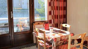 A dining area with a table set for two, a window with curtains, and a view of buildings outside. - Studio for 4 near slopes in Vars (Vars)