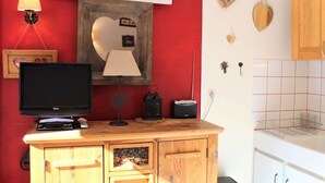 A room with a wooden cabinet, a television, a lamp, a mirror, and decorative items on the wall. - Studio for 4 near slopes in Vars (Vars)