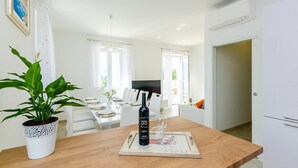 Een eetgedeelte met een houten tafel gedekt voor twee personen, een fles wijn en een menukaart. Links staat een potplant en in de achtergrond is een andere eettafel zichtbaar.
