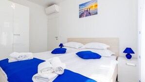 Een hotelkamer met een bed, witte muren, een schilderij van een zonsondergang, een blauwe lamp en een witte nachtkastje.