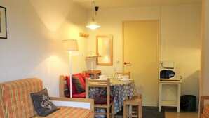A small, cozy living room with a sofa, a dining table with chairs, a microwave, and a lamp.