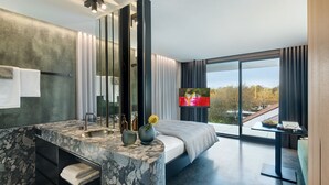 A modern hotel room with a marble bathroom, a large bed, a TV, and a balcony with a city view. - Appartement Hotel Royal (Bad Fuessing)
