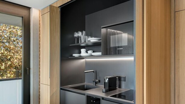 A modern kitchen with dark cabinetry, a built-in oven, and a stainless steel sink. - Appartement Hotel Royal (Bad Fuessing)