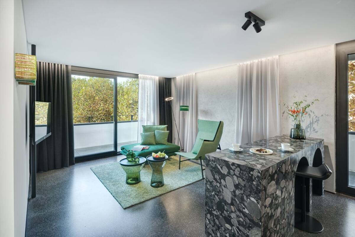 A modern living room with a green sofa, a marble coffee table, and a dining area with a table and chairs.