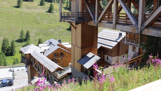Un chalet de montagne en bois, à plusieurs niveaux, doté d’un balcon et offrant une vue sur une vallée verdoyante.